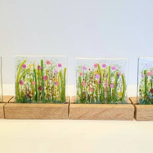 May include: Four square glass panels with a painted design of pink and yellow flowers in a green field. Each panel is mounted on a small wooden stand.
