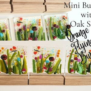 May include: Three small glass tiles with colorful images of orange flying bugs and ladybugs in a green grassy field. The tiles are on small wooden stands. The text "Mini Bug Tiles with Oak Stands Orange Flying Bugs" is in the upper right corner of the image.