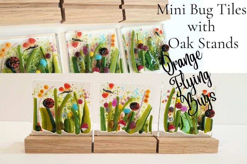 May include: Three small glass tiles with colorful images of orange flying bugs and ladybugs in a green grassy field. The tiles are on small wooden stands. The text "Mini Bug Tiles with Oak Stands Orange Flying Bugs" is in the upper right corner of the image.
