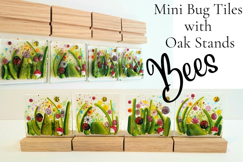 May include: Five small glass tiles with a nature scene of green grass, flowers, mushrooms, and bees. The tiles are displayed on wooden stands. The text "Mini Bug Tiles with Oak Stands Bees" is written above the tiles.