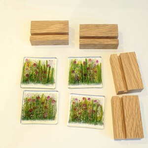 May include: Four glass coasters with a floral design featuring pink flowers and green foliage. The coasters are displayed on four wooden stands.