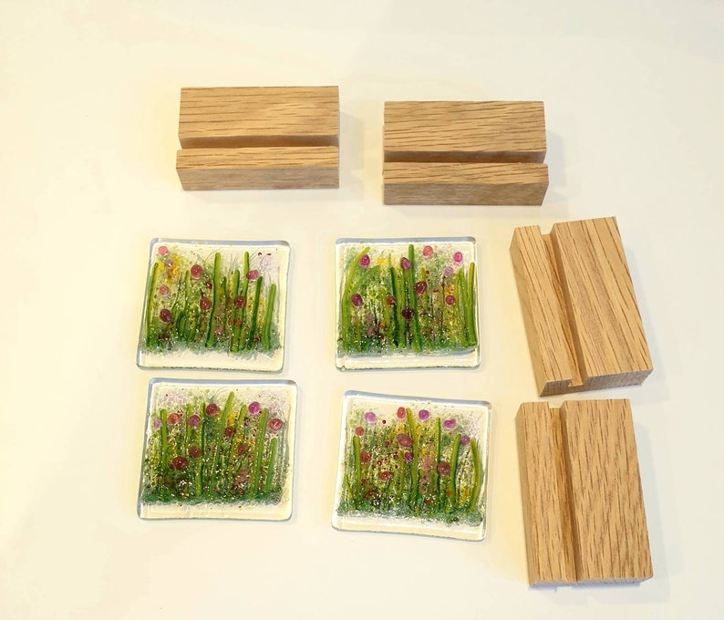 May include: Four glass coasters with a floral design featuring pink flowers and green foliage. The coasters are displayed on four wooden stands.