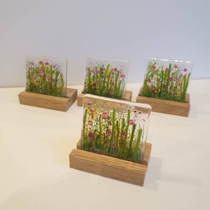 May include: Four square glass pieces with a floral design in shades of pink, green, and yellow, each mounted on a wooden stand.
