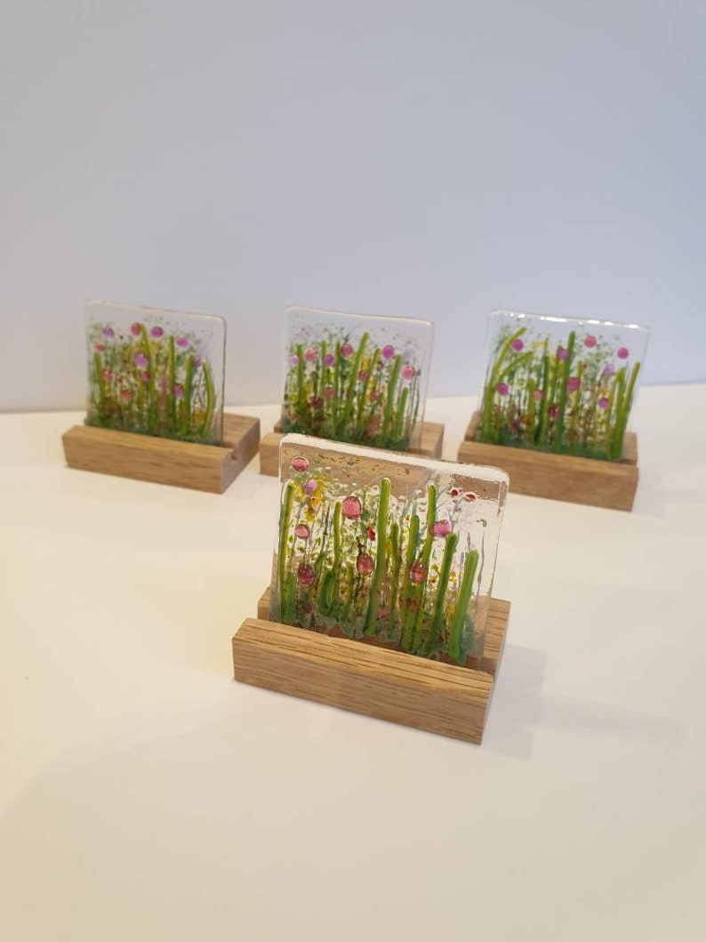 May include: Four square glass pieces with a floral design in shades of pink, green, and yellow, each mounted on a wooden stand.