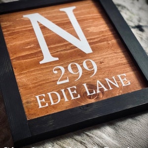 May include: Wooden framed sign with a stained finish. The sign displays the letter "N", the number "299", and the words "EDIE LANE" in white lettering. The frame is black, and the text "Single Stained Option" is at the bottom.