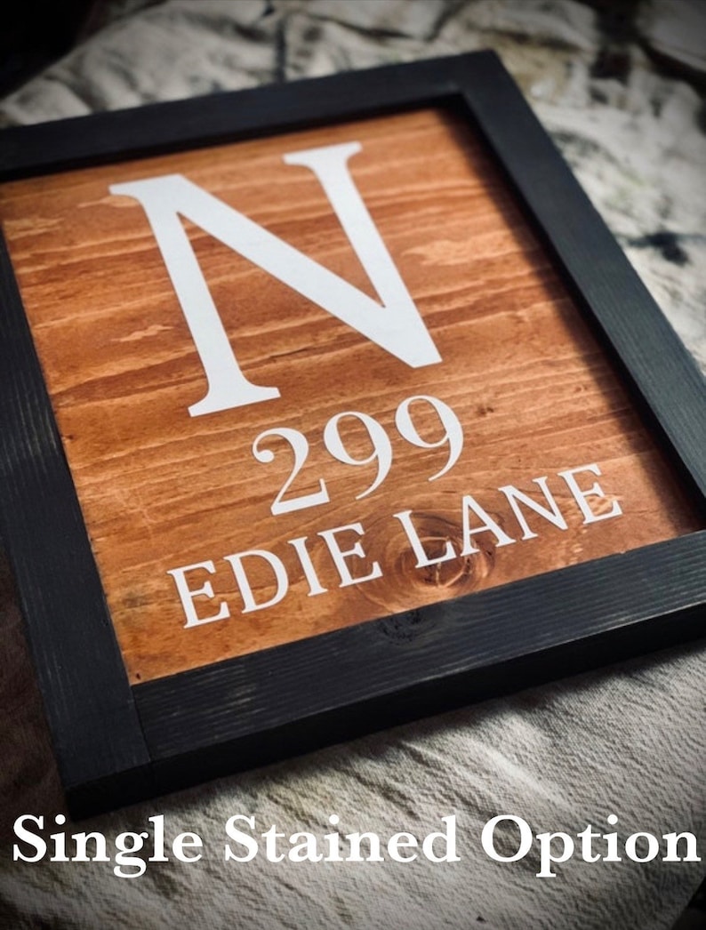 May include: Wooden framed sign with a stained finish. The sign displays the letter "N", the number "299", and the words "EDIE LANE" in white lettering. The frame is black, and the text "Single Stained Option" is at the bottom.