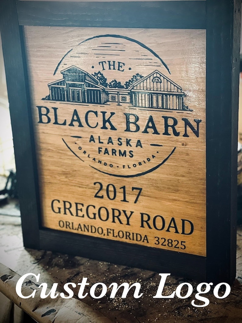May include: Wooden sign in a black frame. The sign displays the text "THE BLACK BARN ALASKA FARMS ORLANDO FLORIDA" and "2017 GREGORY ROAD ORLANDO, FLORIDA 32825". It also includes a custom logo.