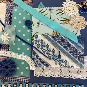 May include: A collection of blue and white fabric scraps, lace, and embellishments. The fabrics feature various patterns, including polka dots, stripes, and floral designs. There are also two blue crocheted flowers and a white crocheted snowflake.