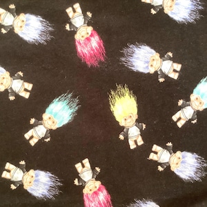 May include: Black fabric with a repeating pattern of cartoon troll dolls. The trolls have colorful hair in shades of blue, pink, and yellow. They wear white shirts and black jackets. The dolls are in various positions.