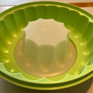 May include: A green plastic mold with a fluted edge and a white plastic center insert. The mold is designed for making a ring-shaped dessert.