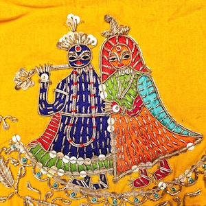 May include: Embroidered textile featuring two figures in traditional attire. The figures are adorned with intricate details, including blue, red, green, and orange embroidery, and silver embellishments. The background is a vibrant yellow.