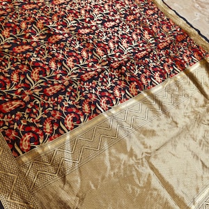 May include: A detailed shot of a textile with a floral pattern. The fabric features a dark navy blue background with a repeating pattern of red and gold floral designs. A gold border with geometric patterns frames the edge.