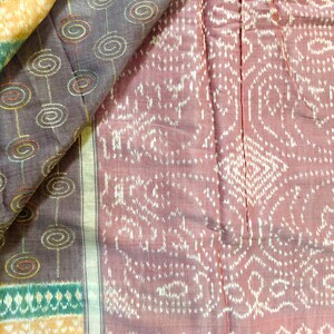 May include: Close-up of a folded textile with intricate patterns. The fabric features a combination of colours, including shades of purple, pink, yellow, and green. The design includes spiral and geometric shapes, creating a visually rich texture.