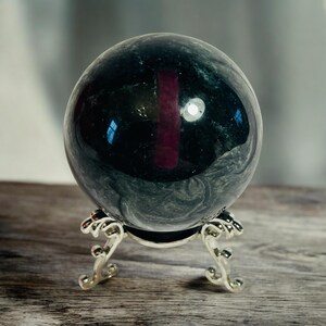 May include: A black and grey marble sphere on a silver stand. The sphere is polished and reflects light.