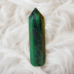 May include: A green and black crystal point with a pointed tip and a smooth, polished surface.