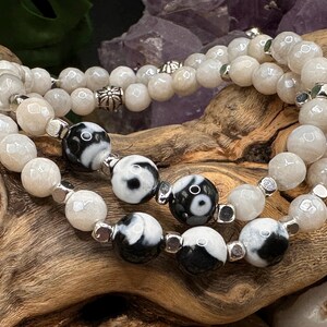 May include: A double-strand beaded bracelet featuring faceted off-white stone beads and smooth black and white yin-yang patterned beads. The design includes small silver-toned metal spacers and decorative floral-shaped metal beads throughout.