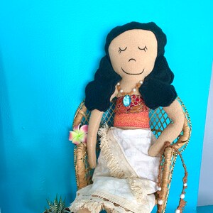 Peut inclure: Une poup&eacute;e faite &agrave; la main habill&eacute;e en Moana du film Disney Moana. La poup&eacute;e est assise dans un fauteuil en osier avec une fleur dans les cheveux. Elle porte une jupe blanche, un haut rouge et orange et un collier bleu.