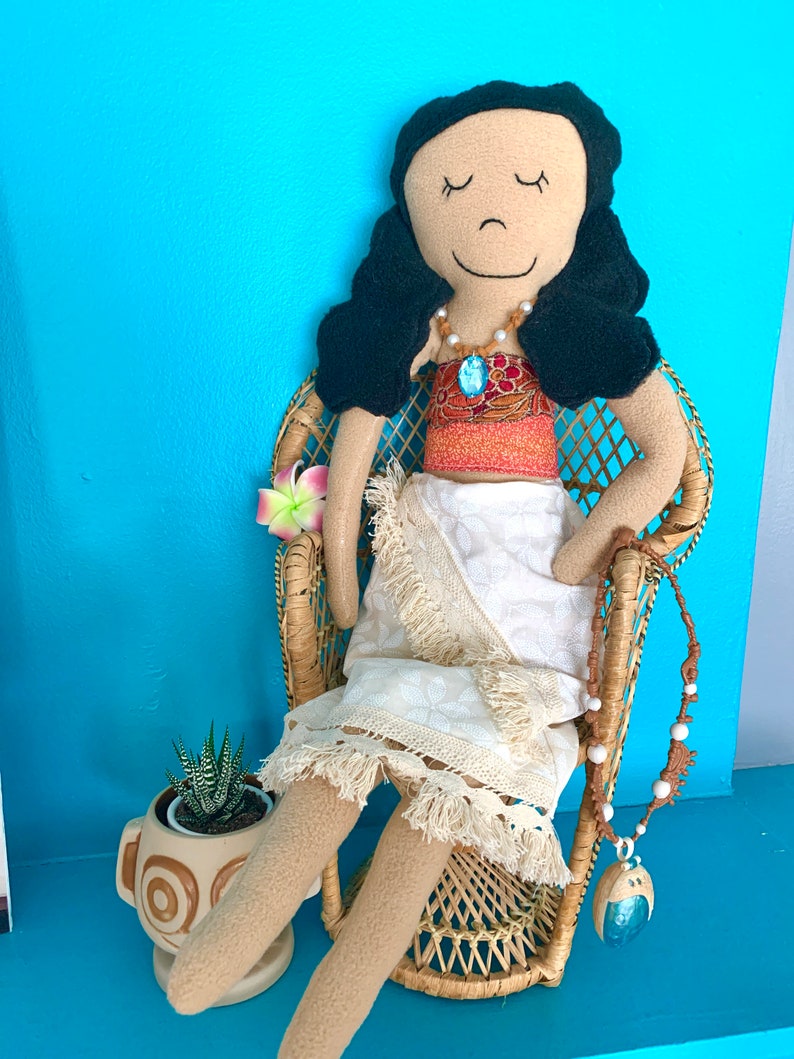 Peut inclure: Une poup&eacute;e faite &agrave; la main habill&eacute;e en Moana du film Disney Moana. La poup&eacute;e est assise dans un fauteuil en osier avec une fleur dans les cheveux. Elle porte une jupe blanche, un haut rouge et orange et un collier bleu.