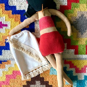 Peut inclure: Une poup&eacute;e faite &agrave; la main avec des cheveux noirs, une jupe rouge et une jupe blanche &agrave; franges. La poup&eacute;e est allong&eacute;e sur un tapis color&eacute;.