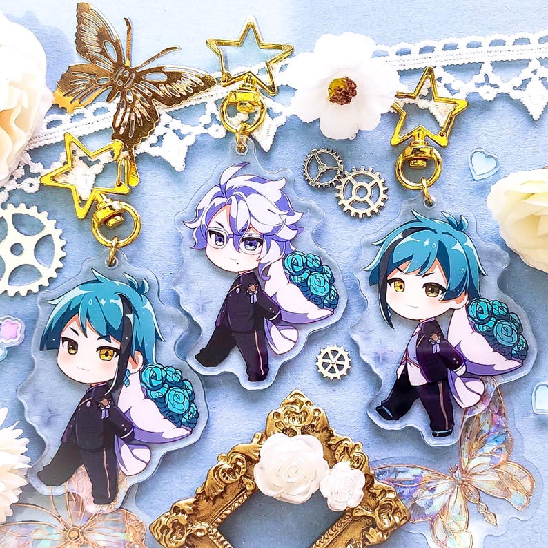 Op de afbeelding: Drie anime-personagecharms met gouden sleutelhangers. De charms zijn van helder acryl met kleurrijke illustraties van personages met blauw, wit en groen haar. Elke charm heeft een witte achtergrond met een bloemmotief.