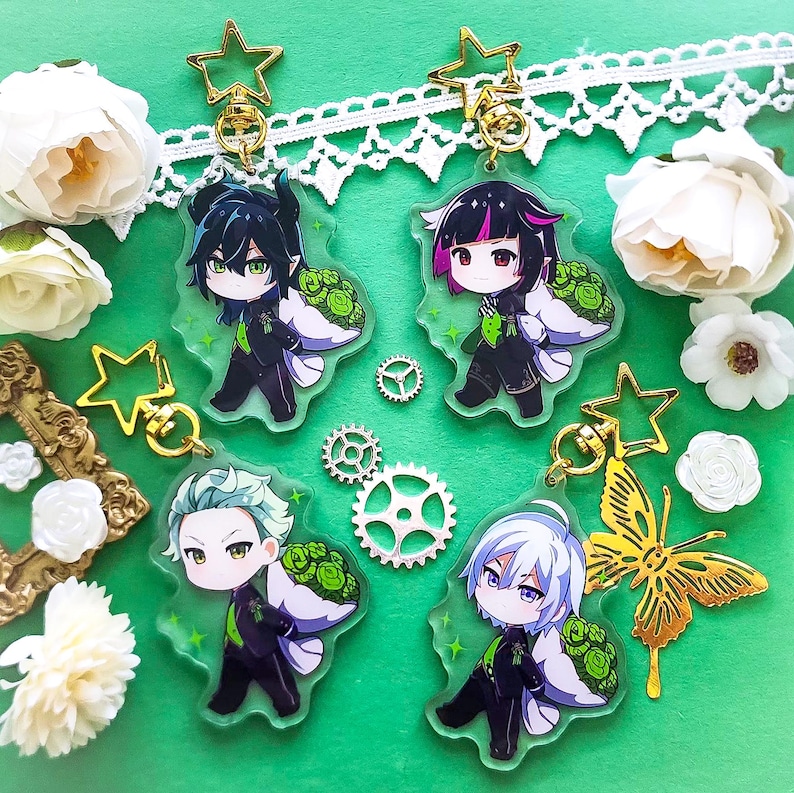 Op de afbeelding: Vier kleurrijke anime-personage sleutelhangers met groene bloemmotieven. Elke sleutelhanger heeft een ander personage met zwart haar, groene ogen en een zwart-witte outfit. De sleutelhangers zijn bevestigd aan gouden metalen ringen en stervormige bedels.