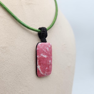 May include: A rectangular pink and white stone pendant suspended from a black macrame knot on a green cord. The stone features a marbled texture with irregular white veins running through the pink surface, secured by a black cord necklace.