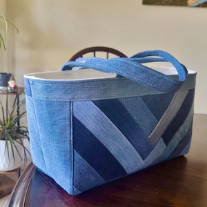 Può includere: Una borsa tote in denim blu con un motivo a chevron. La borsa ha due manici ed è realizzata in denim riciclato.
