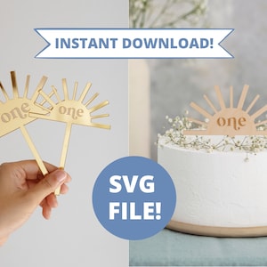May include: Two gold sunburst cake toppers with the word "one" in a retro font. The toppers are on sticks and are shown in a hand and on a white cake.