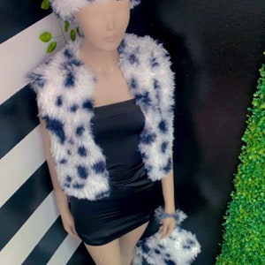 May include: A black and white fuzzy vest, headband, and leg warmers. The vest has a dalmatian-like pattern. The headband and leg warmers are also black and white.