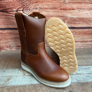 May include: A pair of brown leather work boots with a white rubber sole. The boots have a pull-on tab and a red logo on the side.
