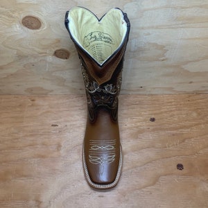 Op de afbeelding: Bruine leren cowboylaarzen met gouden borduurwerk en een vierkante neus. De laarzen hebben een trek-op-stijl en een gevoerde binnenzool. De binnenkant van de laars is gevoerd met een cr&egrave;mekleurige stof en heeft een label met de tekst "La Se&ntilde;a Boots".