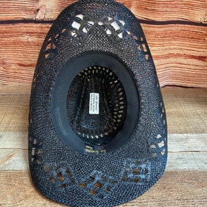 May include: Black straw cowboy hat with a floral cutout design. The hat has a black band and a label that reads "La Siesta Cotton Polyester Made in Mexico".
