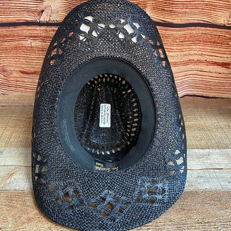May include: Black straw cowboy hat with a floral cutout design. The hat has a black band and a label that reads "La Siesta Cotton Polyester Made in Mexico".