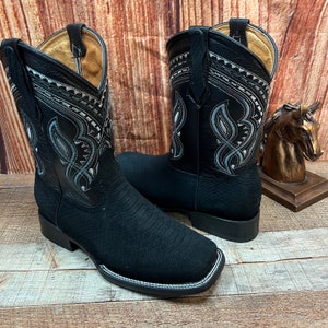 May include: A pair of black leather cowboy boots with a decorative silver stitching design. The boots have a pointed toe and a low heel.