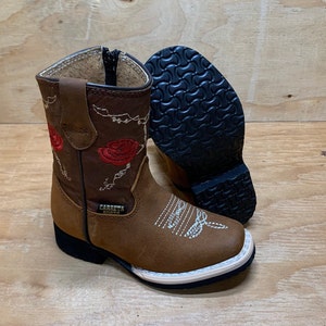 May include: Brown leather children's cowboy boots with red embroidered roses and a white stitching detail. The boots have a black rubber sole and the text "CARRETH BOOTS" is printed on the side.