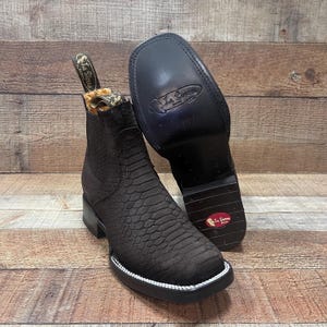 May include: Dark brown leather ankle boots with a textured, snake-like pattern. The boots have a square toe, a white trim, and a black sole. The brand name "La Sierra" is visible on the pull tab and sole.