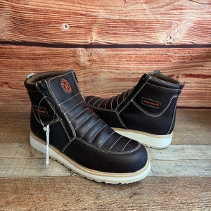 May include: A pair of brown leather boots with a zipper on the side. The boots have a white sole and a black stitching detail. The boots have the text "ARCO BOOTS" on the side.