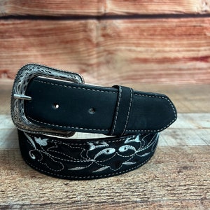 May include: A black leather belt with a silver buckle and white embroidery. The embroidery features a floral design.
