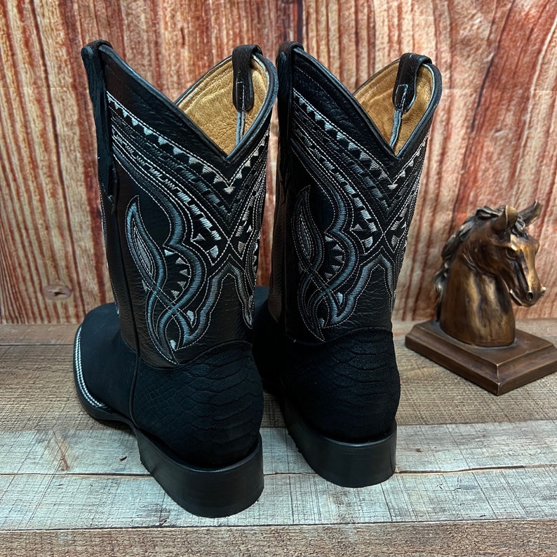 May include: A pair of black leather cowboy boots with intricate silver stitching on the shaft. The boots have a pointed toe and a stacked heel.
