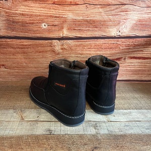 May include: A pair of black leather ankle boots with a zipper on the side. The boots have a white stitching detail around the sole and the text "ARCO BOOTS" is printed on the side of the right boot.