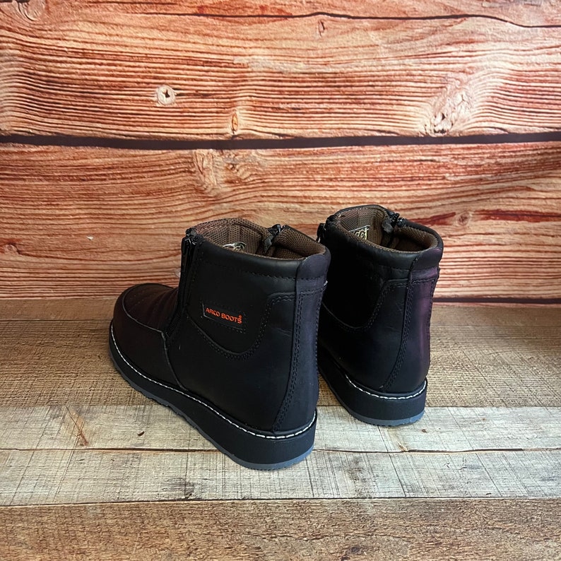 May include: A pair of black leather ankle boots with a zipper on the side. The boots have a white stitching detail around the sole and the text "ARCO BOOTS" is printed on the side of the right boot.