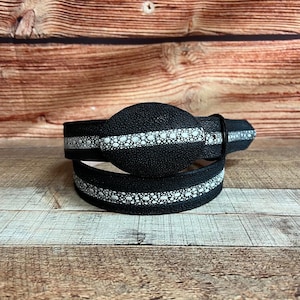 May include: A black belt with a white dotted stripe design. The belt has a textured surface and a silver-colored buckle. The belt is made of a durable material and is suitable for everyday wear.
