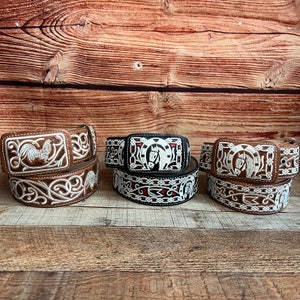 May include: Three leather belts with silver embroidery and different buckle designs. The buckles feature a rooster, a horseshoe with a horse's head, and a horseshoe with a horse's head.