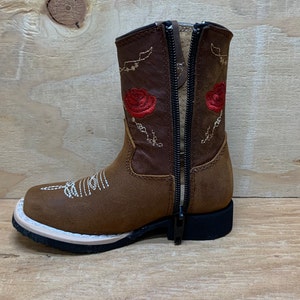 May include: Brown leather children's cowboy boots with red embroidered roses and a zipper on the back.