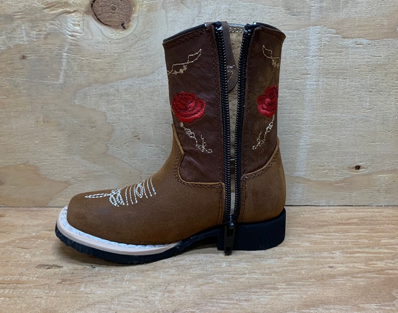 May include: Brown leather children's cowboy boots with red embroidered roses and a zipper on the back.