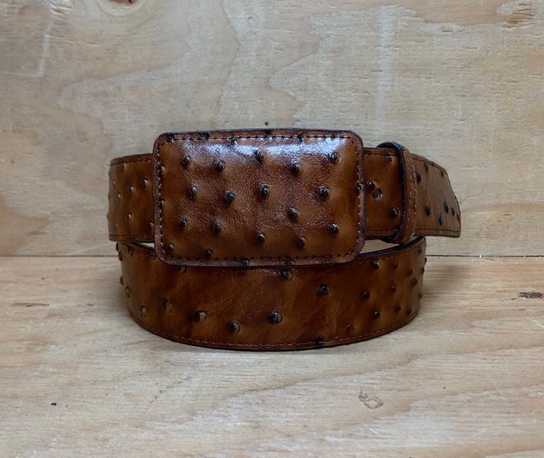 Op de afbeelding: Een bruine leren riem met een struisvogelhuidpatroon en een zilveren gesp.