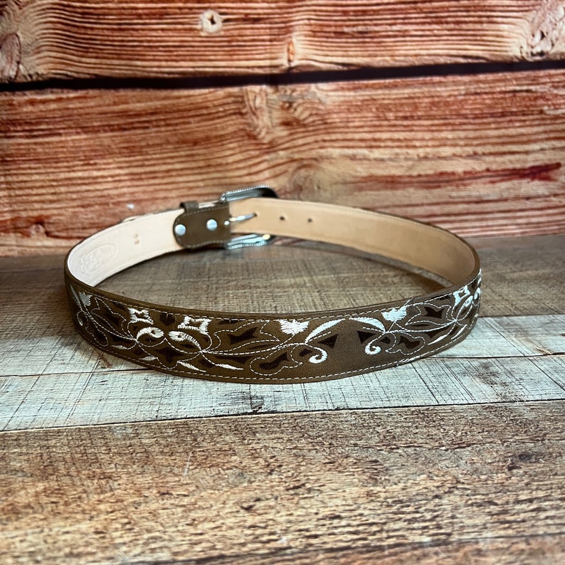 May include: A brown leather belt with a silver buckle and white floral embroidery.