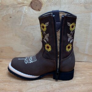 May include: Brown leather boots with a side zipper and embroidered sunflowers. The boots have a pointed toe and a low heel.