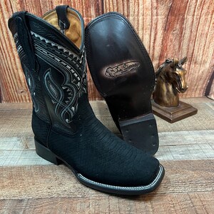 May include: Black leather cowboy boots with a decorative silver design on the shaft. The boots have a pointed toe and a stacked heel. The boots are made by La Sierra.