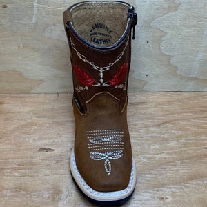 May include: Brown leather children's cowboy boots with red embroidered roses and a zipper on the side. The boots have a white sole and say "Genuine Leather Made in Mexico" on the inside.
